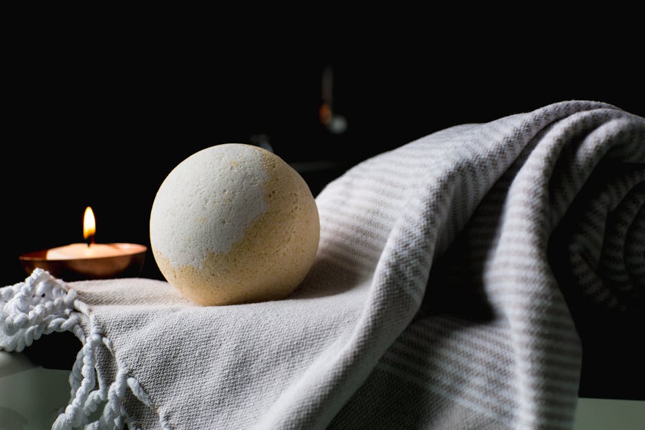 Elegant spa setup featuring a lit candle and a bath bomb on a soft towel